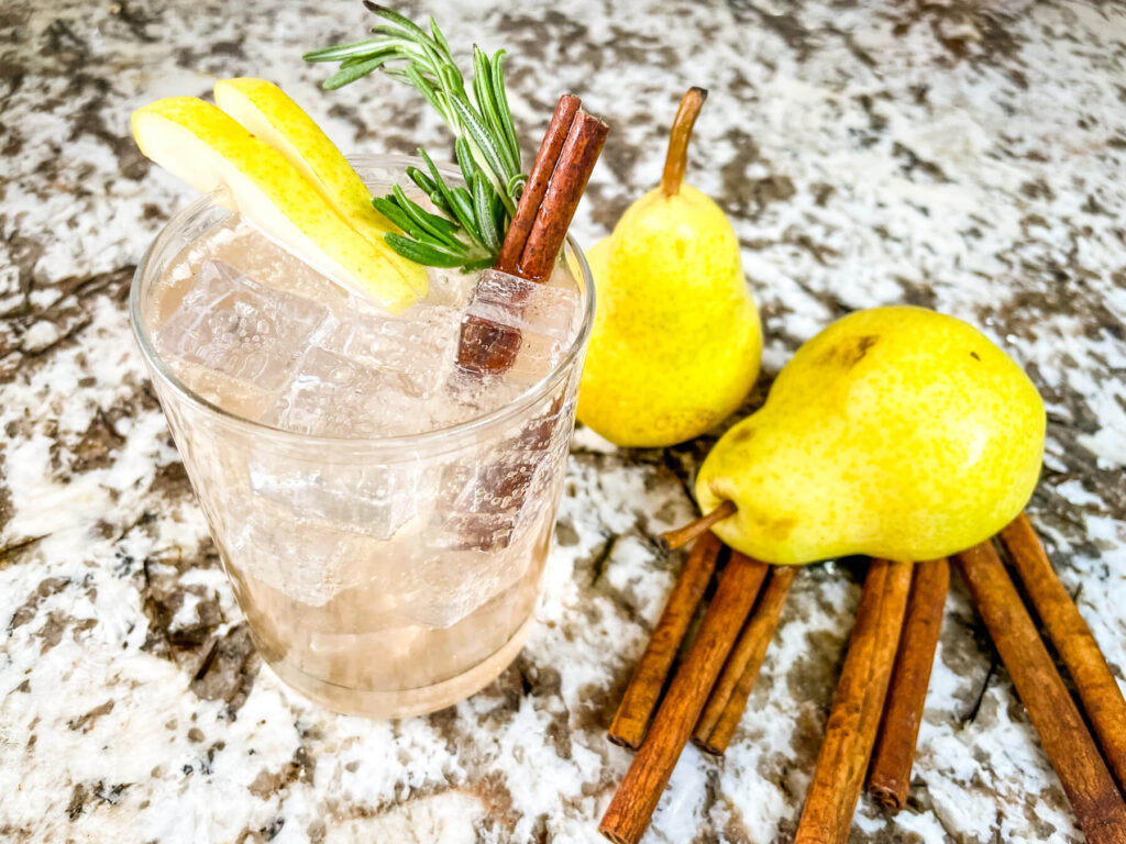 The Pear Tree Vodka Cocktail with pears and cinnamon sticks next to it