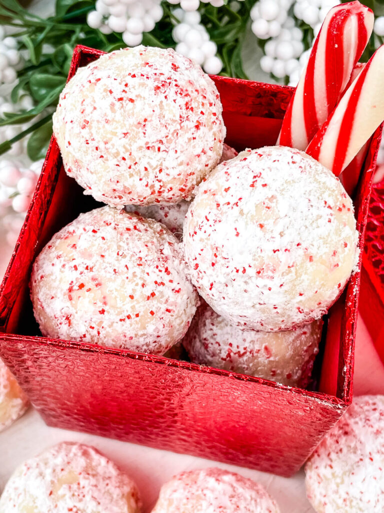 Peppermint Snowball Cookies piled up in a red box with peppermint sticks