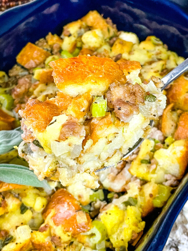A spoon scooping Sausage Stuffing out of a dark blue dish
