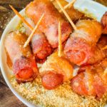 Bacon Wrapped Smokies in a pile on top of sugar mustard mixture on a white round plate