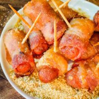 Bacon Wrapped Smokies in a pile on top of sugar mustard mixture on a white round plate