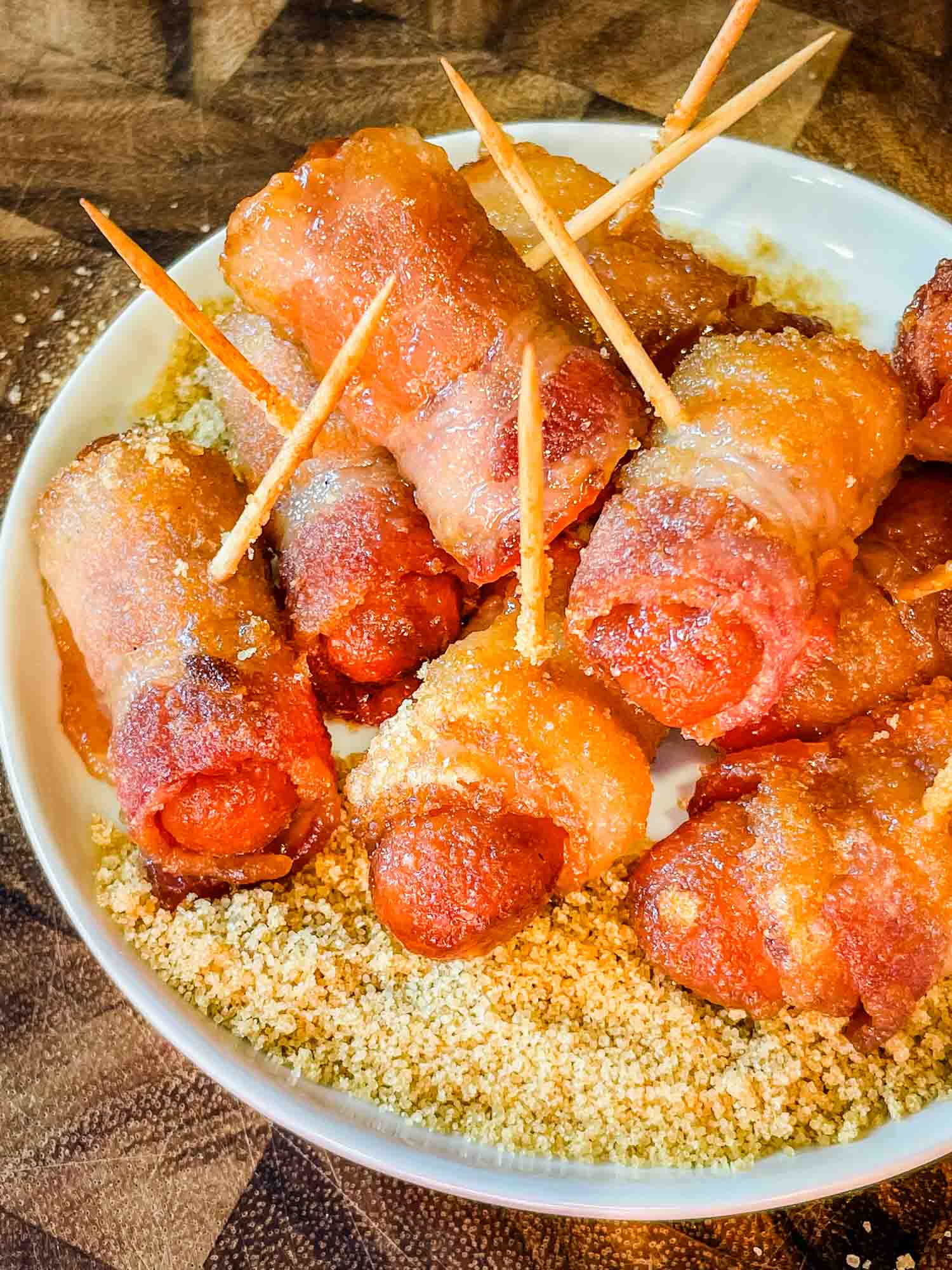 Bacon Wrapped Smokies in a pile on top of sugar mustard mixture on a white round plate