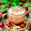 Holly Jolly Christmas Cocktail in a clear mug, topped with chipped cream and surrounded by red ornaments