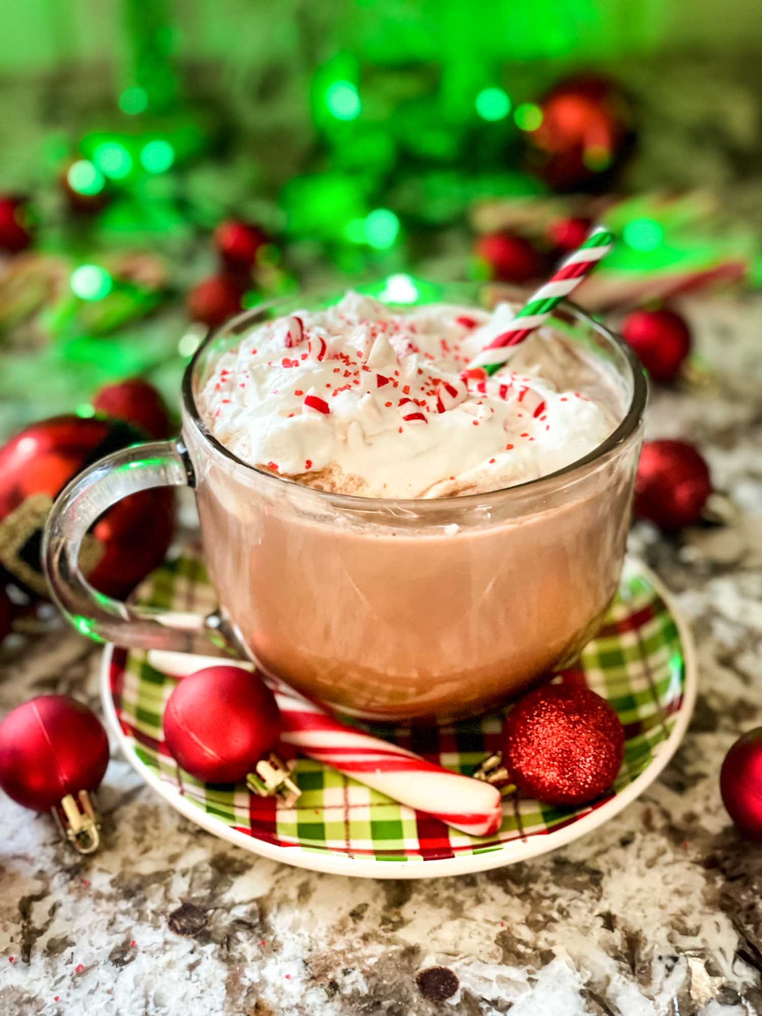 Holly Jolly Christmas Cocktail in a clear mug, topped with chipped cream and surrounded by red ornaments