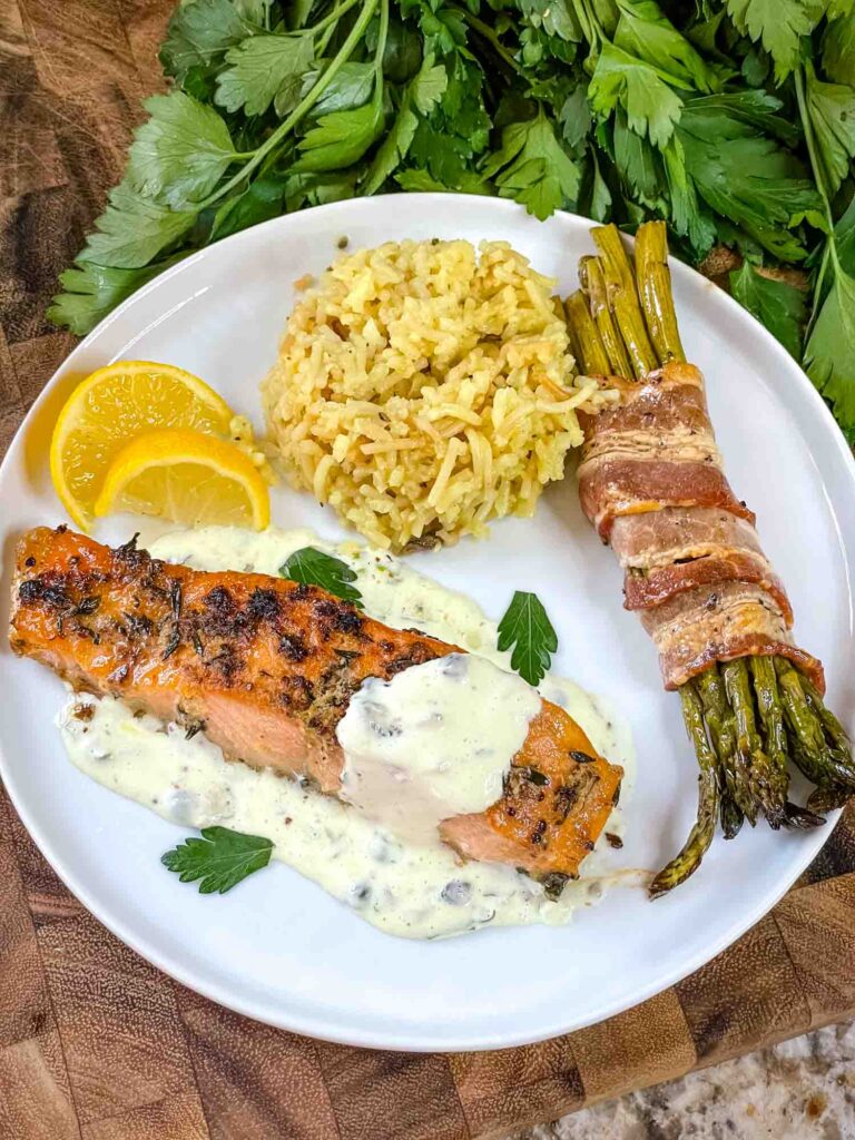 A white plate with Air Fry Salmon, Remoulade Sauce, Asparagus Wrapped in Bacon, and rice