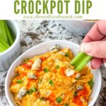 Pin of Buffalo Chicken Crockpot Dip in a bowl with a hand dipping celery into it and title at top