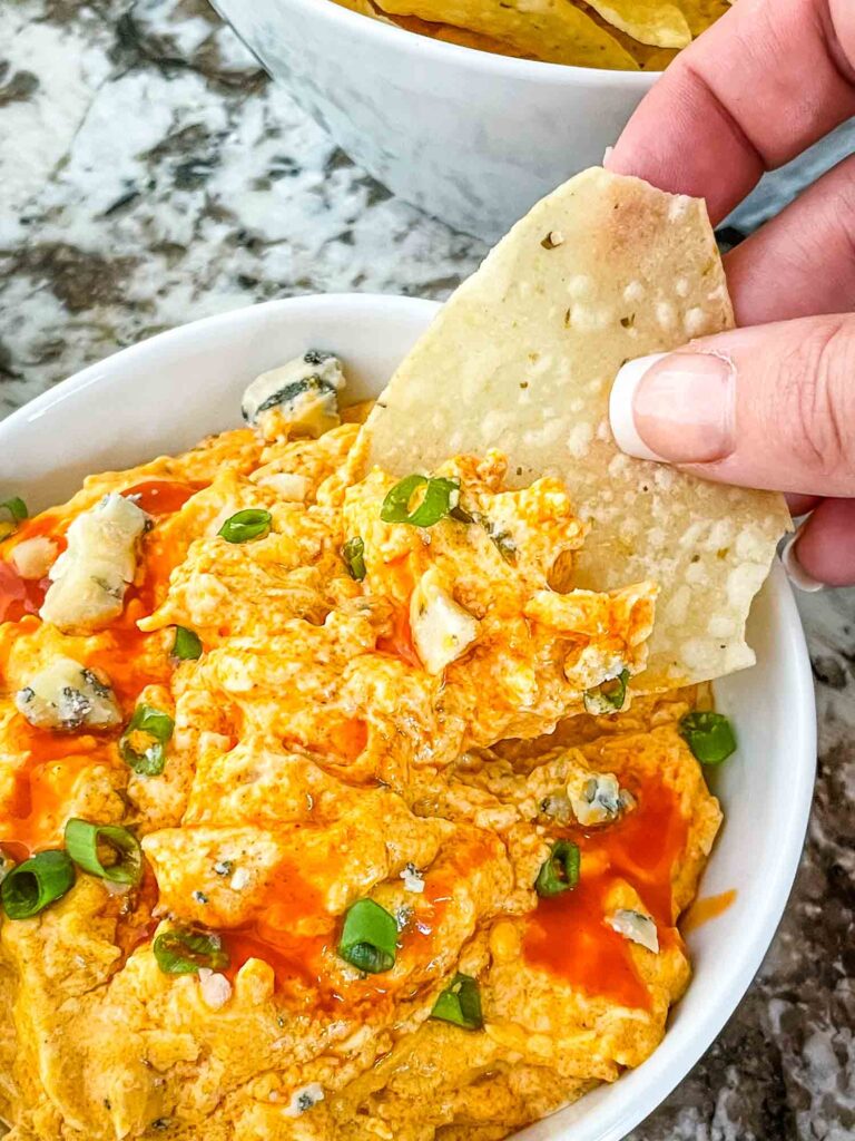 A hand scooping a chip into small bowl of Buffalo Chicken Crockpot Dip