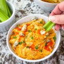 A hand scooping celery into a bowl of Buffalo Chicken Crockpot Dip