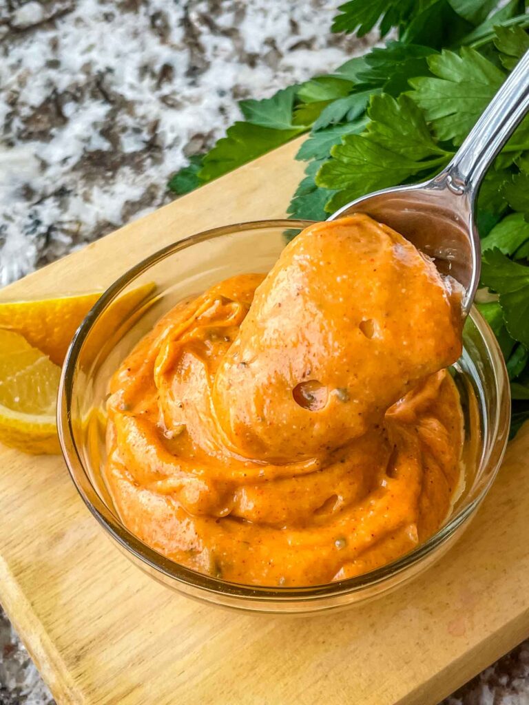 A spoon scooping into a small clear bowl of Cajun Sauce on a cutting board