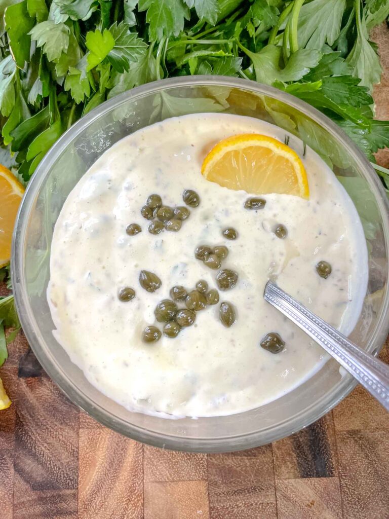 Remoulade Sauce in a bowl with capers and lemon on top and parsley around it