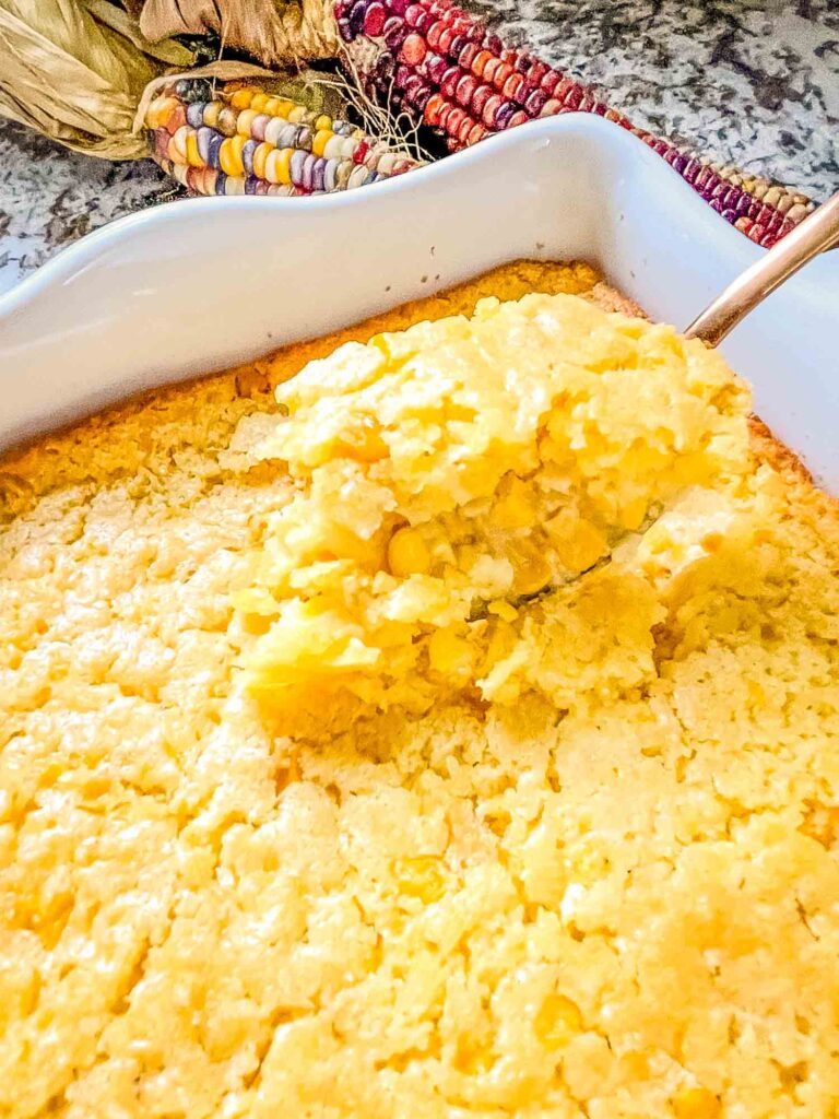 A copper spoon scooping Corn Casserole out of a white dish
