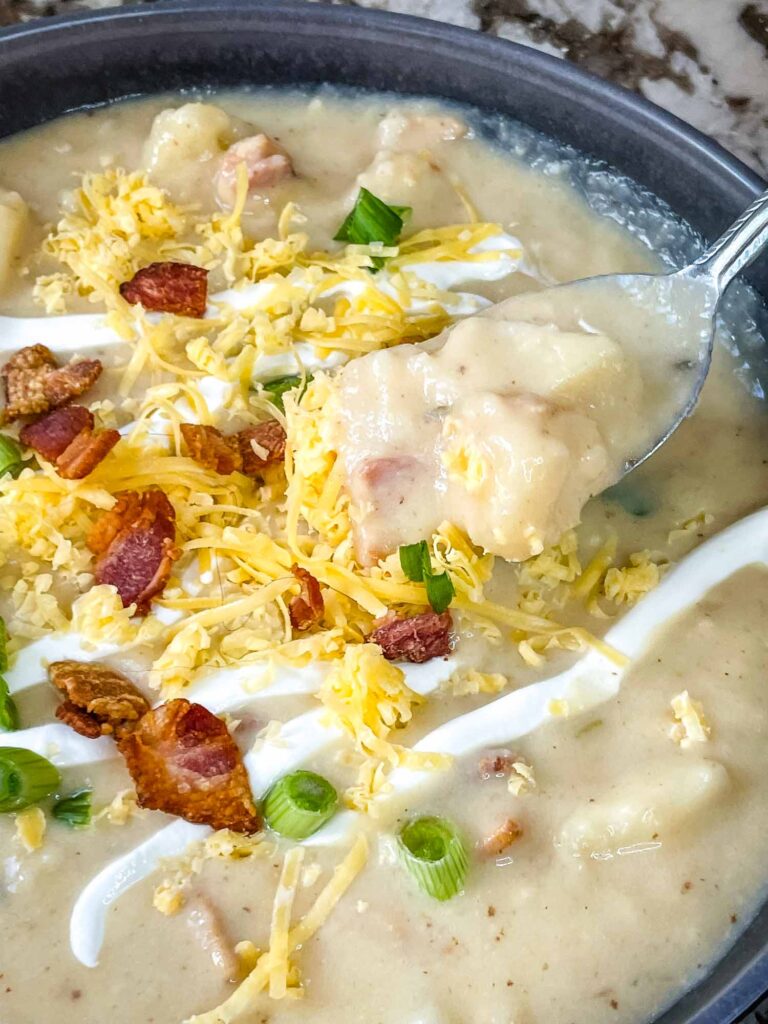 A spoon digging into a bowl of Instant Pot Potato Soup with toppings
