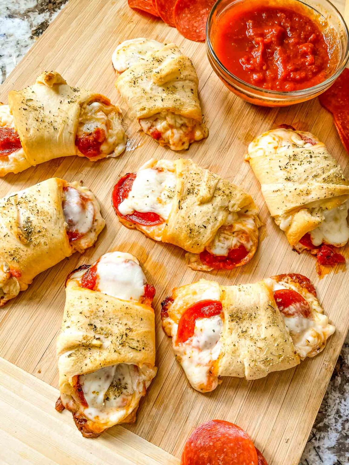 Pizza Crescent Rolls on a cutting board with a bowl of sauce.