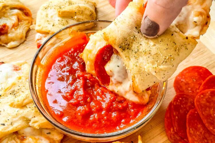 A hand dunking a roll into extra sauce