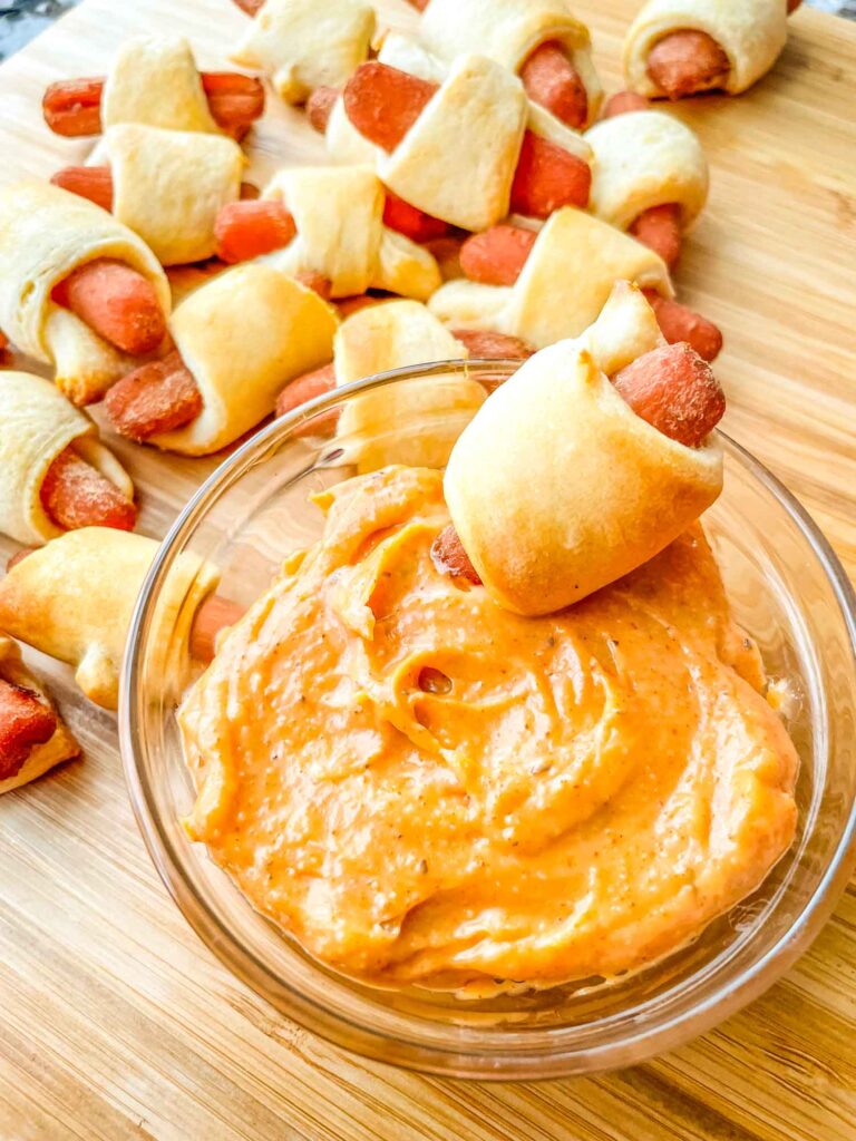 Vegan Carrot Pigs in a Blanket in a pile with one being dunked into Cajun sauce