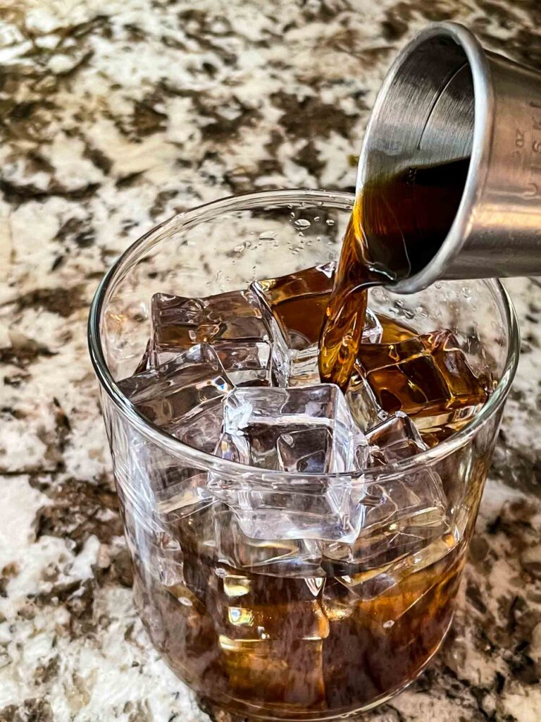 A jigger pouring liquid into the glass