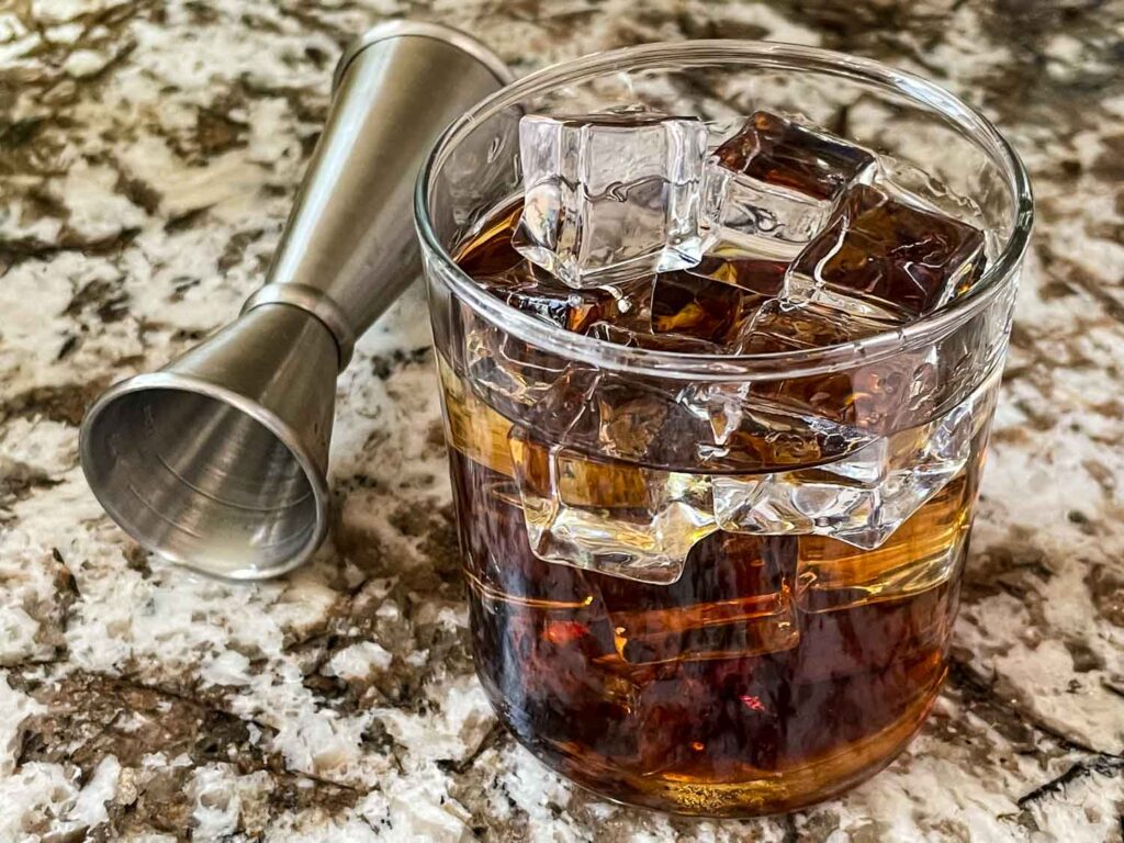 A Black Russian Cocktail in a glass with a jigger next to it