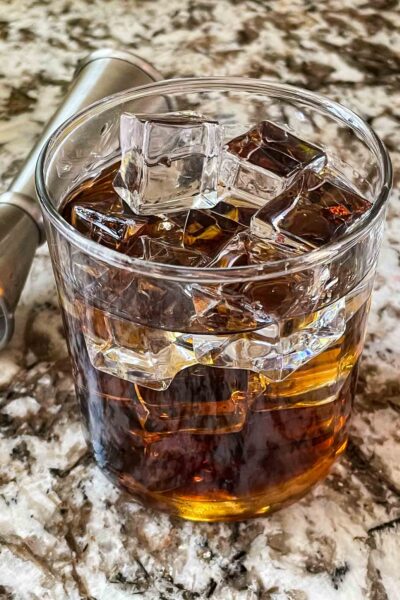 A glass of Black Russian Recipe with a jigger behind it