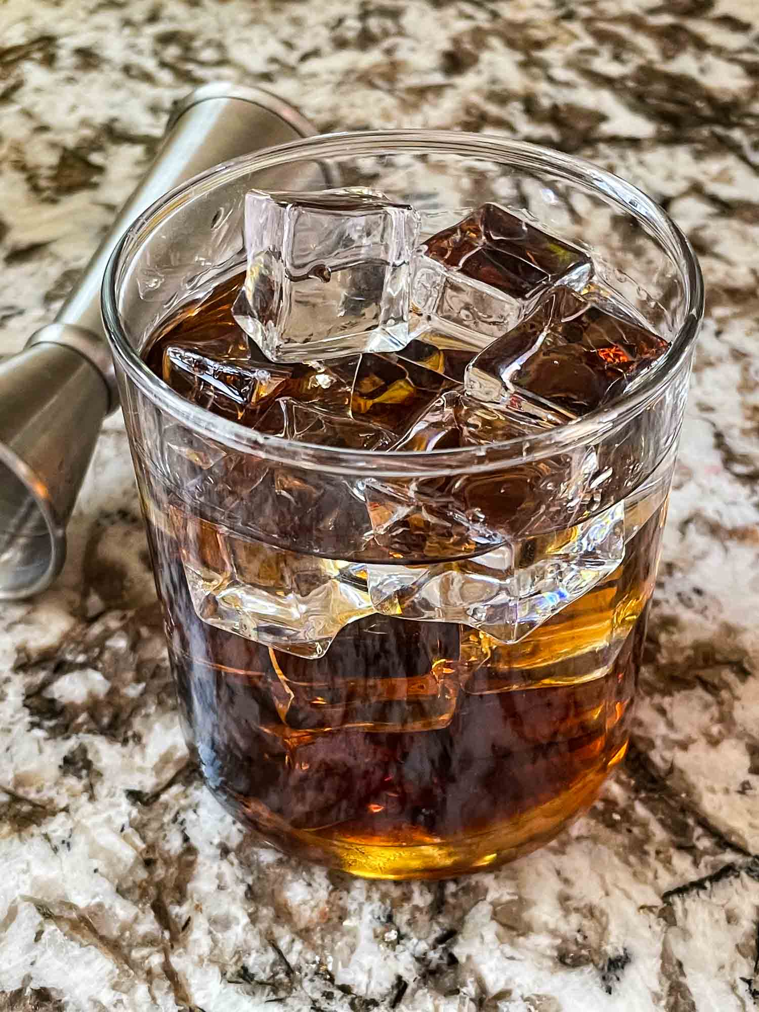 A glass of Black Russian Recipe with a jigger behind it