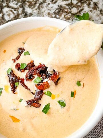 A spoon scooping into a bowl of Creamy Sundried Tomato Sauce