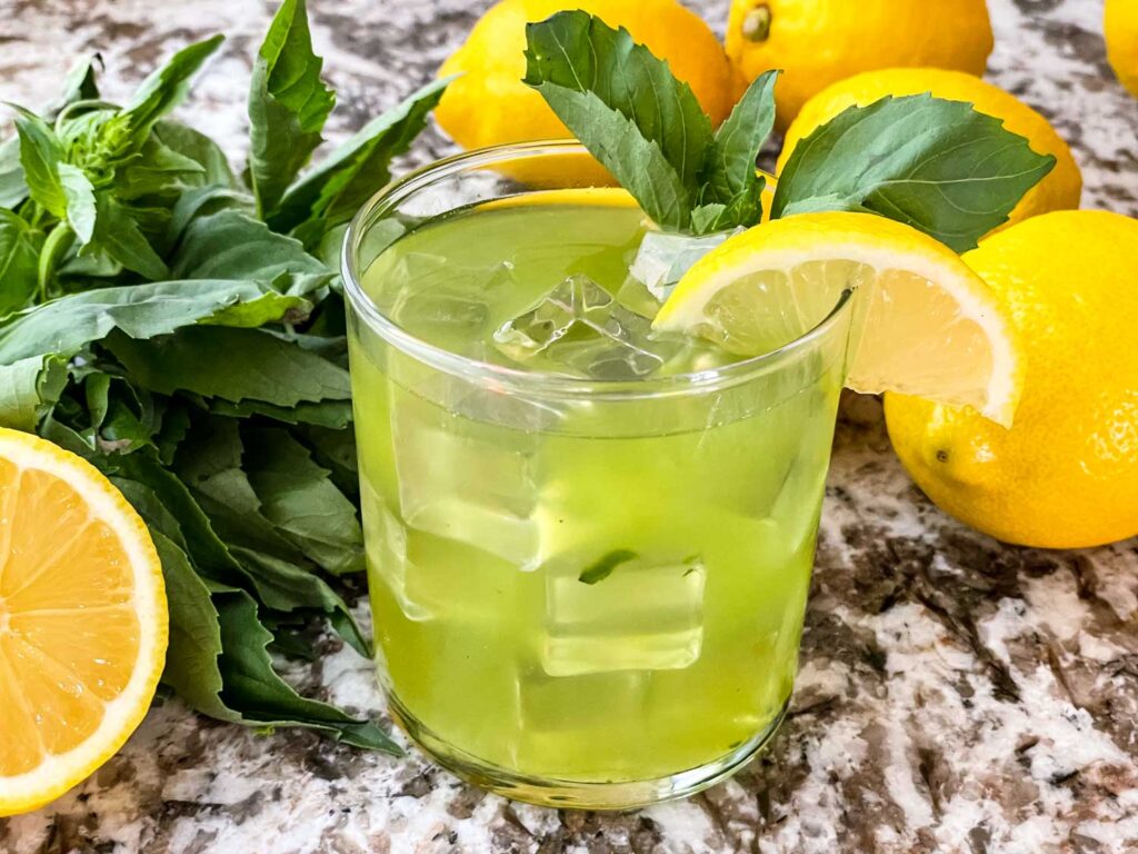 Gin Basil Smash in a glass with lemons and basil around it