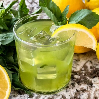 A glass of Gin Basil Smash with basil and lemons around it