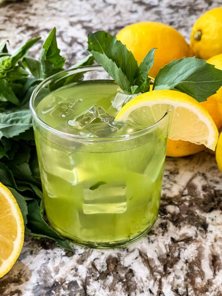 A glass of Gin Basil Smash with basil and lemons around it