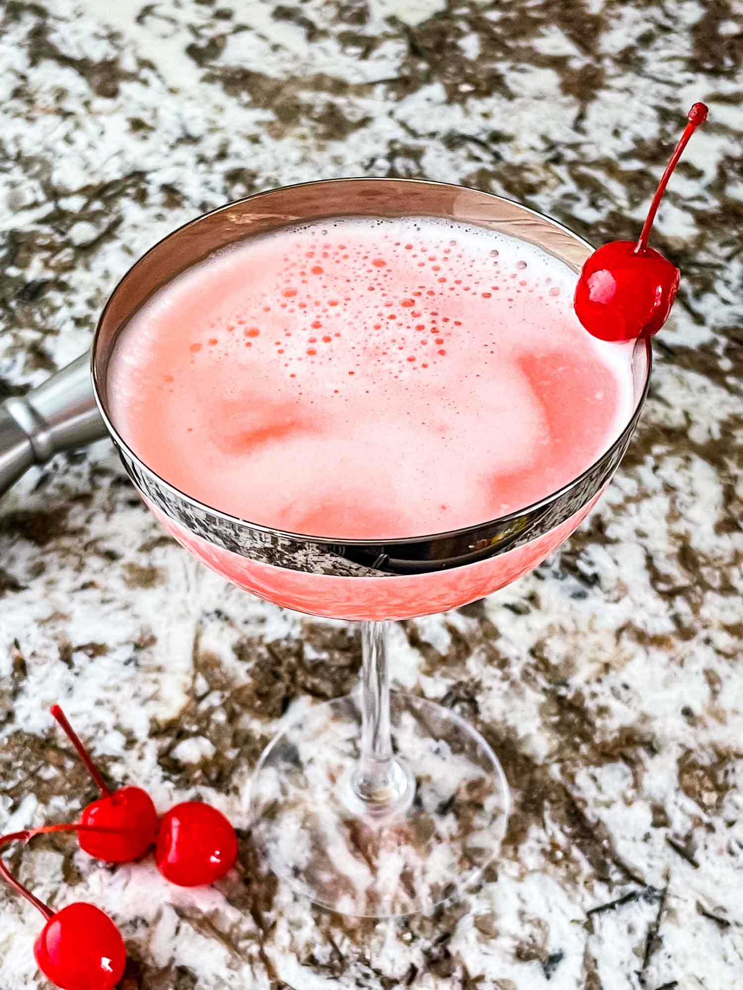 Pink Lady Three Olives Branch a-pink-drink-with-a-lemon-slice-on-the-rim-in-front-of-a-red-background