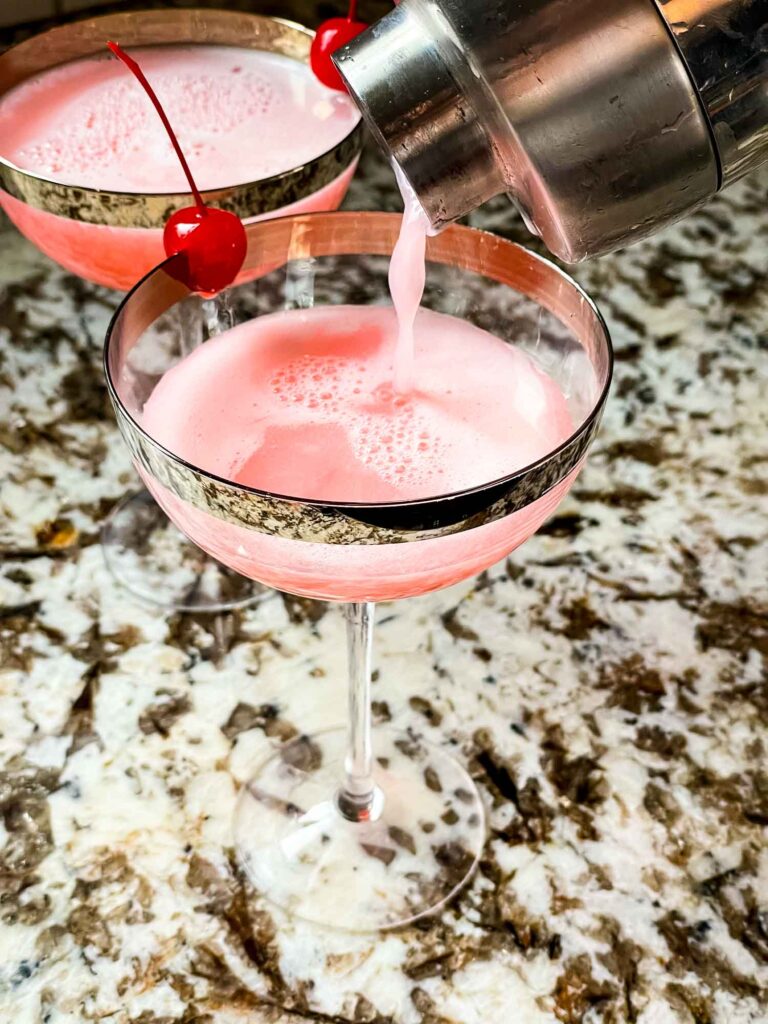 A shaker pouring the cocktail into a glass