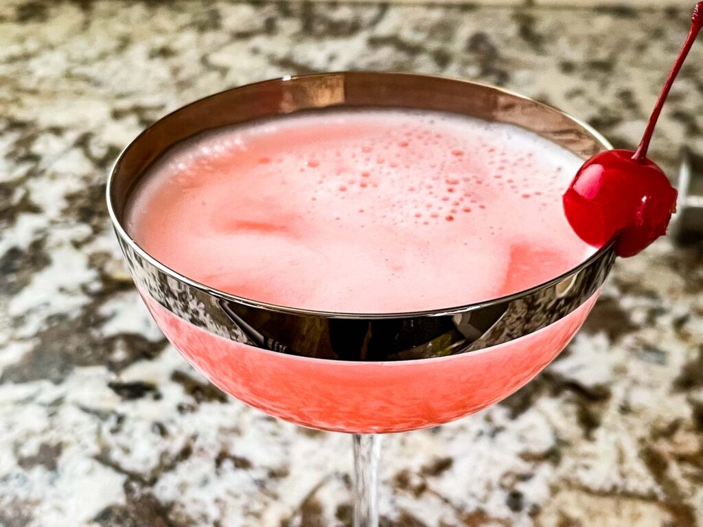 Pink Lady Cocktail in a coupe glass with a cherry