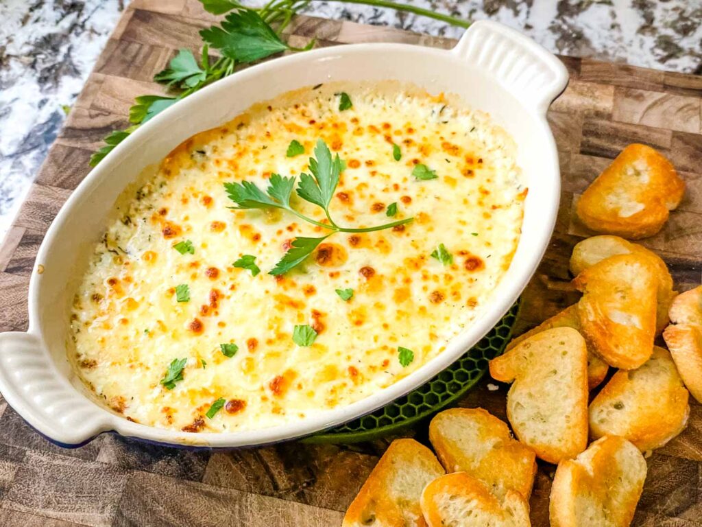 A dish of Copycat Olive Garden Smoked Mozzarella Fonduta with crostini next to it on a cutting board