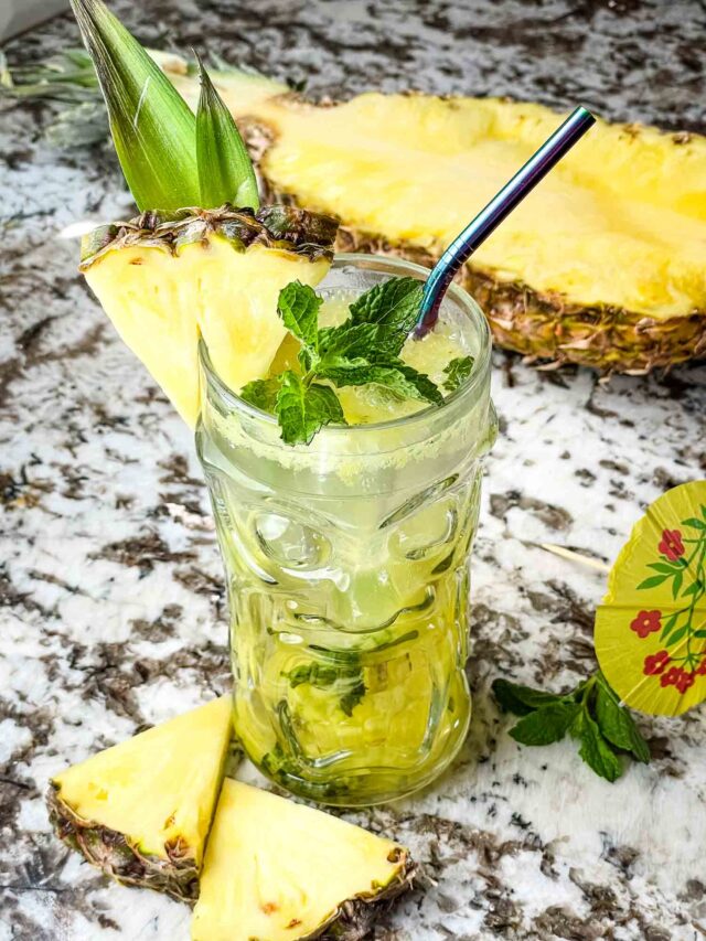 A clear tiki glass filled with Pineapple Mojito and fruit around it