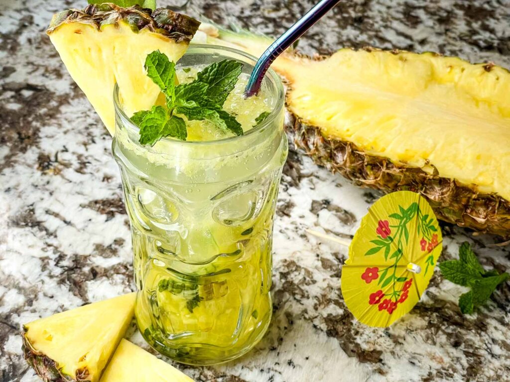 Pineapple Mojito in a clear tiki glass surrounded by pieces of pineapple