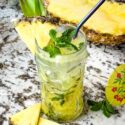 A clear tiki glass filled with Pineapple Mojito and fruit around it