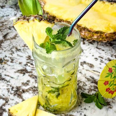 A clear tiki glass filled with Pineapple Mojito and fruit around it