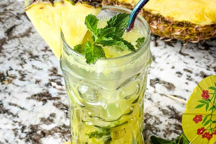 A clear tiki glass filled with Pineapple Mojito and fruit around it