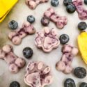 Frozen Blueberry Banana Dog Treats scattered on a counter surrounded by fruit