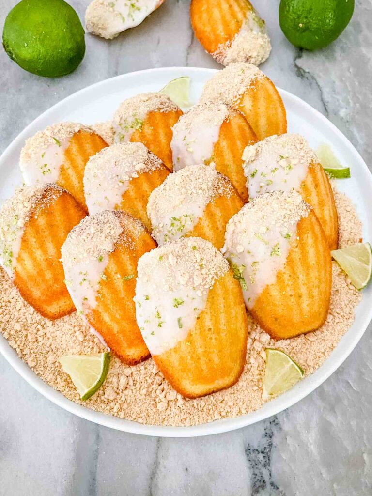 Key Lime Pie Madeleines stacked on a plate with graham cracker crumbs under them