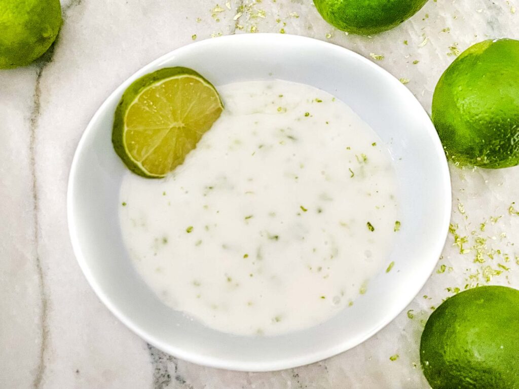 A white bowl filled with Lime Glaze surrounded by limes