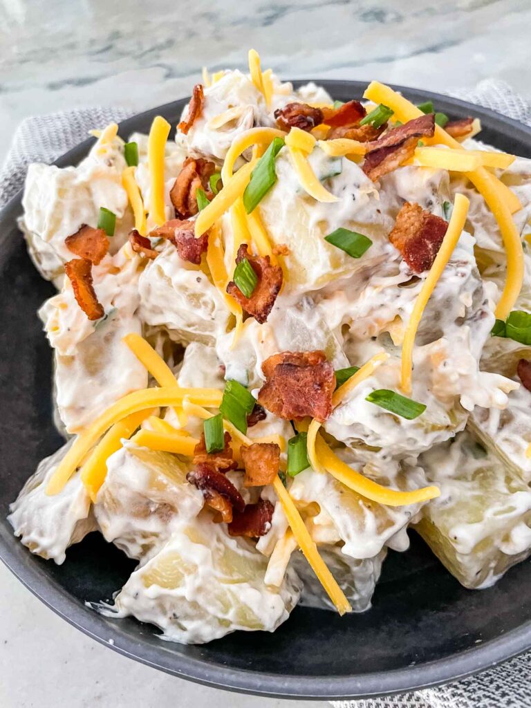 Loaded Potato Salad in a gray bowl with bacon, cheese, and green onions on top