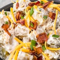 A close up of the Loaded Potato Salad with cheese, bacon, and green onions on top