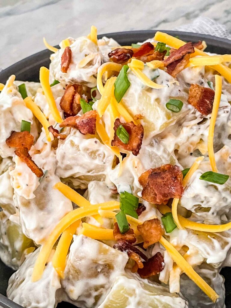 A close up of the Loaded Potato Salad with cheese, bacon, and green onions on top