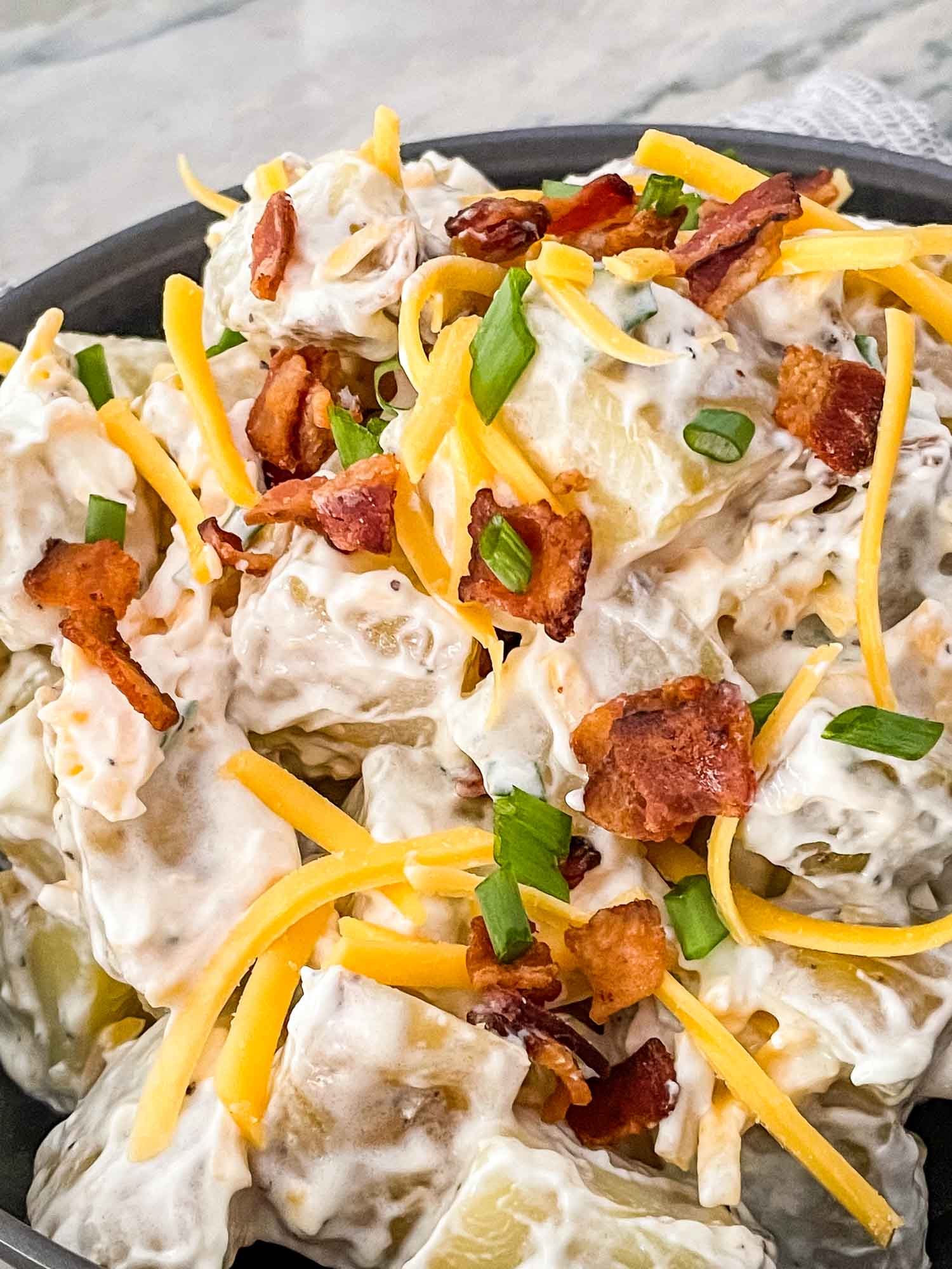 A close up of the Loaded Potato Salad with cheese, bacon, and green onions on top