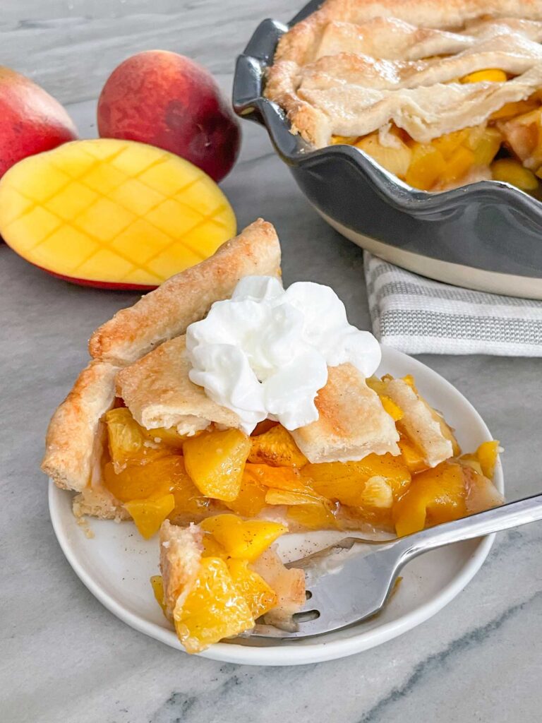 A piece of Peach Mango Pie with whipped cream on a small plate