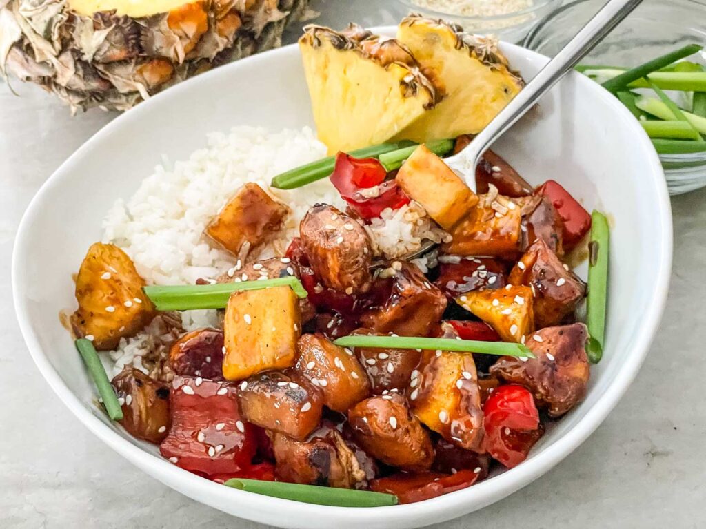 A white bowl filled with Pineapple Chicken and white rice, with a fork in it