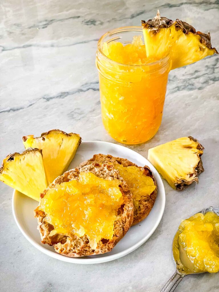 Pineapple Jam in a jar and on muffins surrounded by fruit pieces