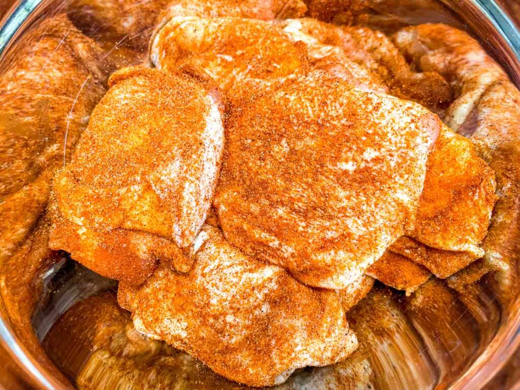 Raw chicken being coated with rub in a bowl