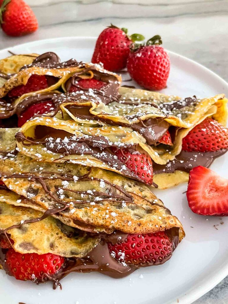 Close up of Strawberry Nutella Crepes on a white plate with extra strawberries around them