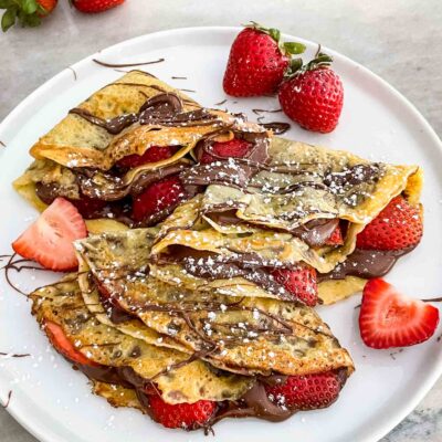 Strawberry Nutella Crepes on a white plate and garnished with more chocolate and fruit
