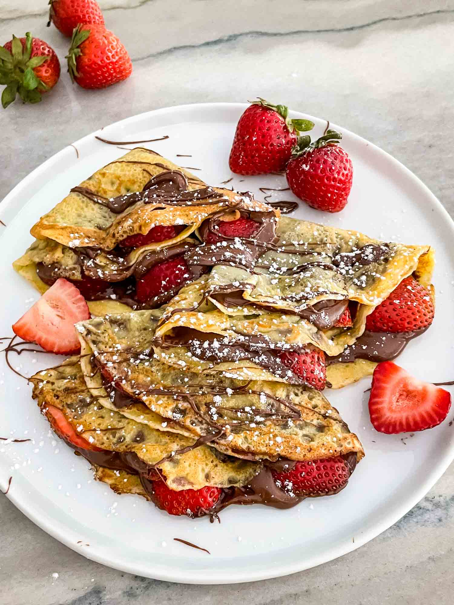 Strawberry Nutella Crepes on a white plate and garnished with more chocolate and fruit